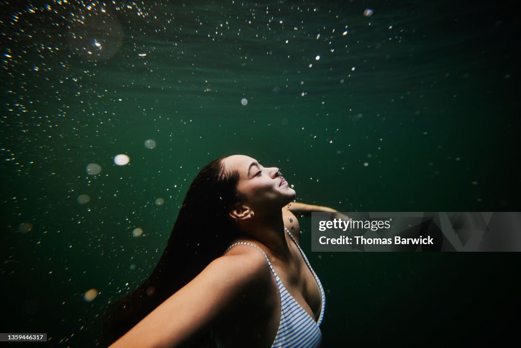 Medium wide shot underwater view of woman swimming underwater in cenote