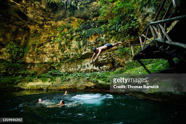 wide shot of man diving into cenote with friends - cenote mexico stock pictures, royalty-free photos & images
