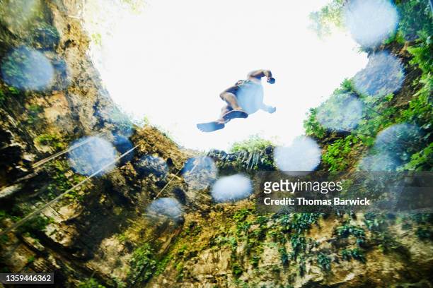 Wide shot low angle view of man jumping from platform into cenote