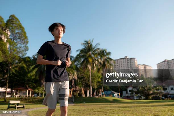 asian chinese teenage boy jogging in public park alone during weekend  morning - running shorts stock pictures, royalty-free photos & images