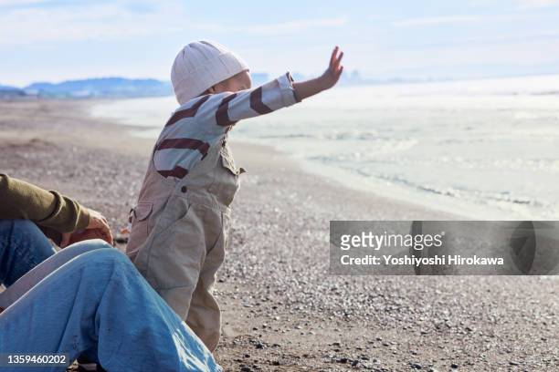 toddlers and genuine parents waving towards horizon of sea - levenslang leren stockfoto's en -beelden