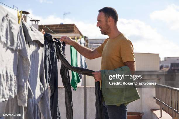 man picking up dry clothes from clothesline to hang up wet clothes. - man hanging stock pictures, royalty-free photos & images