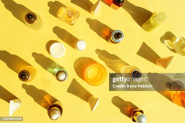 trendy beauty concept with facial serum, natural essential oil, hand cream, lip balm and perfume in cosmetic bottles with dropper and bright sunny shadow on yellow color background. - vitamine c stockfoto's en -beelden