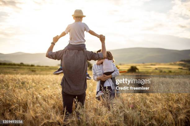happy family spending time in nature and walking across grass field - family standing stock pictures, royalty-free photos & images