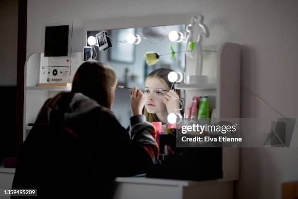 reflection of a teenage girl in an illuminated mirror on a bedroom dressing table, using a mascara wand to apply mascara - bedroom vanity stock pictures, royalty-free photos & images