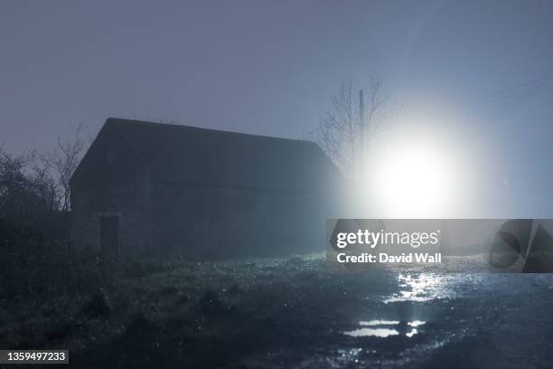 an abandoned barn back lighted on a foggy winters night in the countryside. - barn stock pictures, royalty-free photos & images