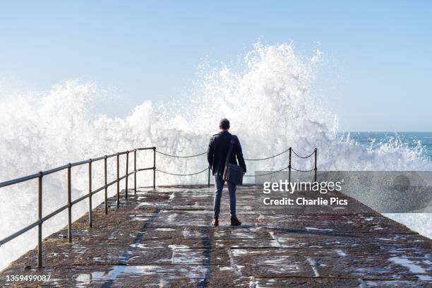 business man on harbour looking out to sea with wave crashing against wall. - south west england fotografías e imágenes de stock