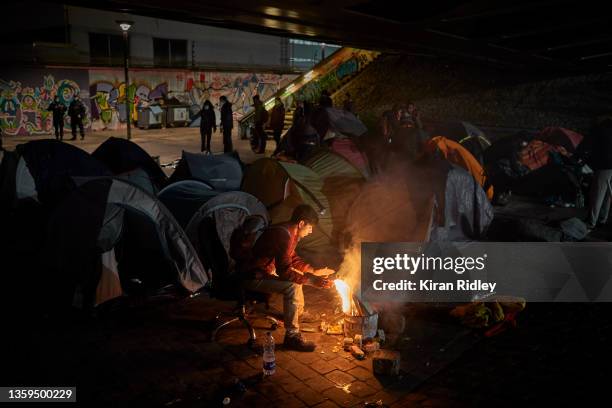 An Afghan migrant sits around a fire to keep warm as their makeshift camp on the outskirts of Paris is evacuated by city officials and police on...