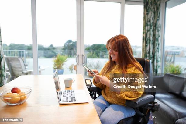 disabled woman at home in wheelchair and using mobile phone. - motorized wheelchair stock pictures, royalty-free photos & images