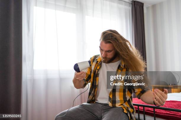 young man with long hair using hairdryer - man combing hair stock pictures, royalty-free photos & images
