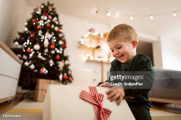 during christmas eve toddler boy opens his christmas present - christmas toys stock pictures, royalty-free photos & images