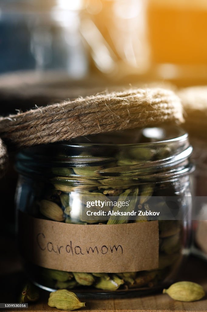 A composition of many different spices and herbs standing in a row on a wooden table or shelf. Dry crushed spices and seasonings in glass jars and containers with inscriptions, in the kitchen cabinet or pantry. The concept of cooking, home decor.