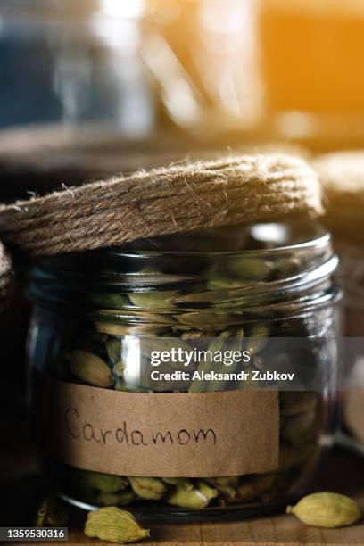 a composition of many different spices and herbs standing in a row on a wooden table or shelf. dry crushed spices and seasonings in glass jars and containers with inscriptions, in the kitchen cabinet or pantry. the concept of cooking, home decor. - cardamom stock-fotos und bilder