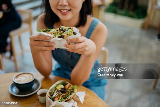 young asian woman eating sandwich in cafe - convenience stock pictures, royalty-free photos & images