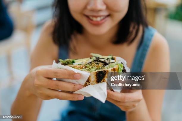 junge asiatin isst sandwich im café - woman sandwich stock-fotos und bilder