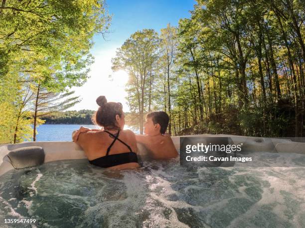 boy and his mom relaxing in a cottage hot tub with a lake view. - bain à remous photos et images de collection