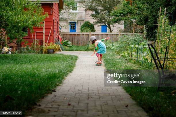 a little girl skateboards down a path through backyard garden - columbus ohio house stock pictures, royalty-free photos & images