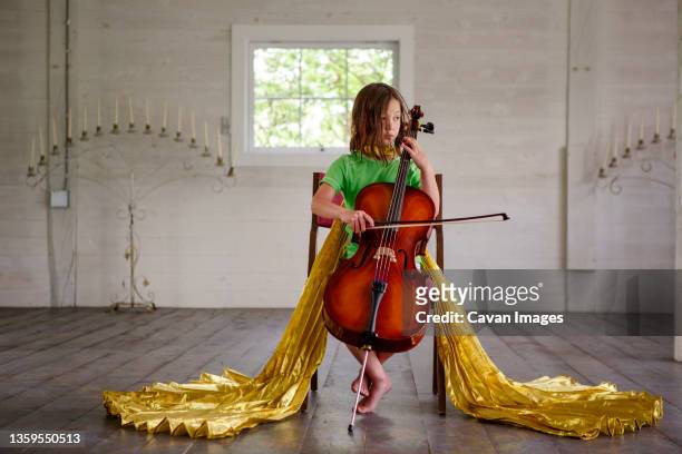 a little girl in long golden wings plays cello in an empty barn - girl cello stock pictures, royalty-free photos & images