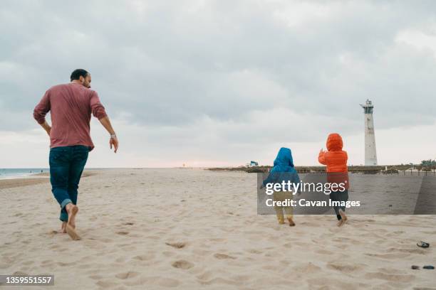 back view of father and children running at beach in canary islands - family sports centre laughing stock pictures, royalty-free photos & images