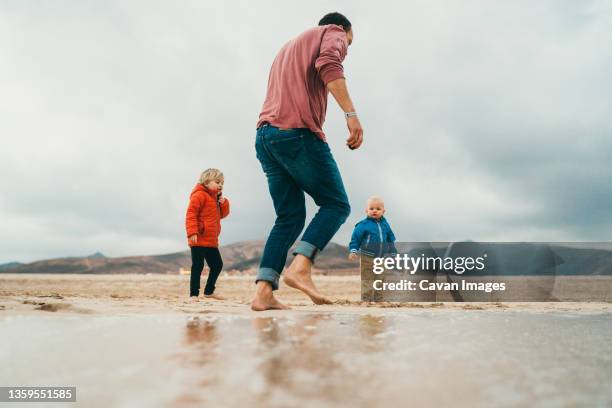 father and sons playing in the sand at beach in canary islands - family sports centre laughing stock-fotos und bilder