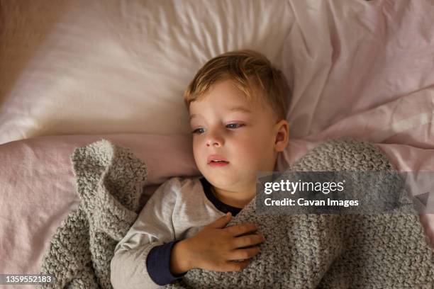 boy lying on bed in pyjama being ill and covered with grey blanket - krankenbett stock-fotos und bilder