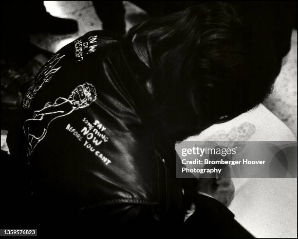 View, from behind, of an unidentified concertgoer, wearing a satin jacket, drawing a picture on the concourse floor at the Bill Graham Auditorium,...