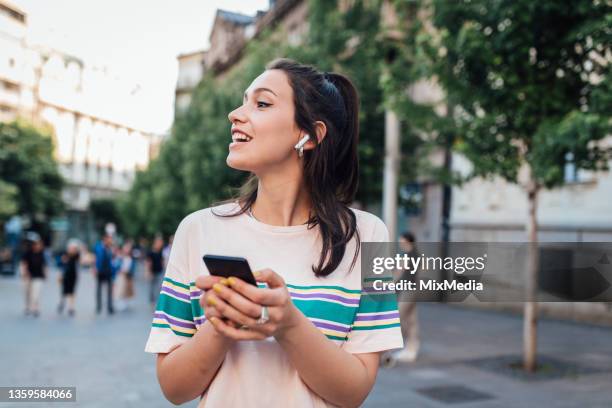 portrait of a happy girl walking down the street and making a video call - bluetooth headphones stock pictures, royalty-free photos & images