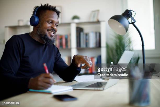 smiling man with headphones having video call on laptop computer in his home office - mid adult men stock pictures, royalty-free photos & images