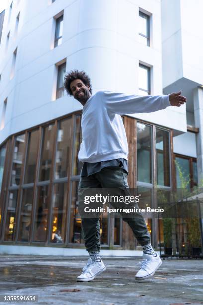 black ethnic man with afro hair and a sweater, modern dance in a white building, movements of the urban dancer man looking at camera - rap battle stock pictures, royalty-free photos & images