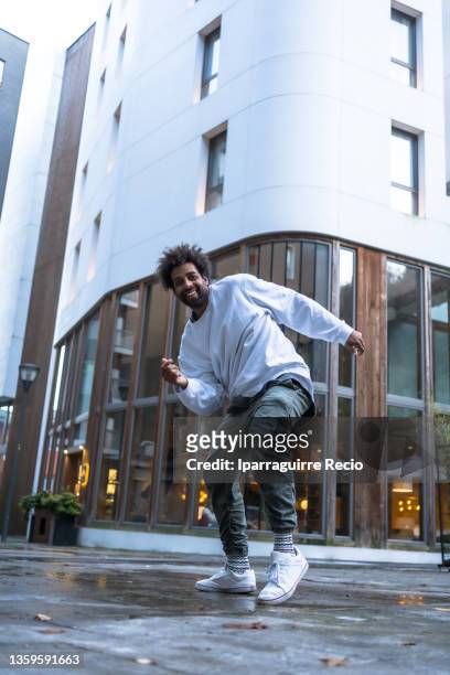 black ethnic man with afro hair and a sweater, modern dance in a white building, movements of the urban dancer man looking at camera - rap ストックフォトと画像