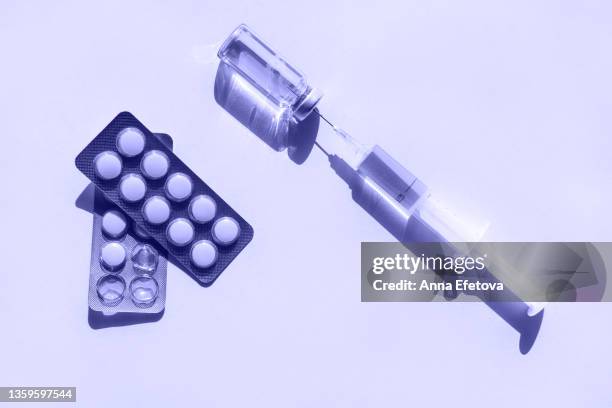 glass vial with a vaccine, disposable syringe and set of blister packs with tablets placed on violet background. photography in flat lay style. demonstrating very peri - color of 2022 year - needle injury stock pictures, royalty-free photos & images