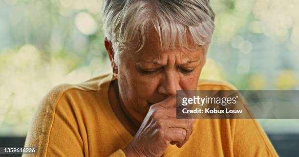 shot of a senior woman coughing at home - tossir imagens e fotografias de stock