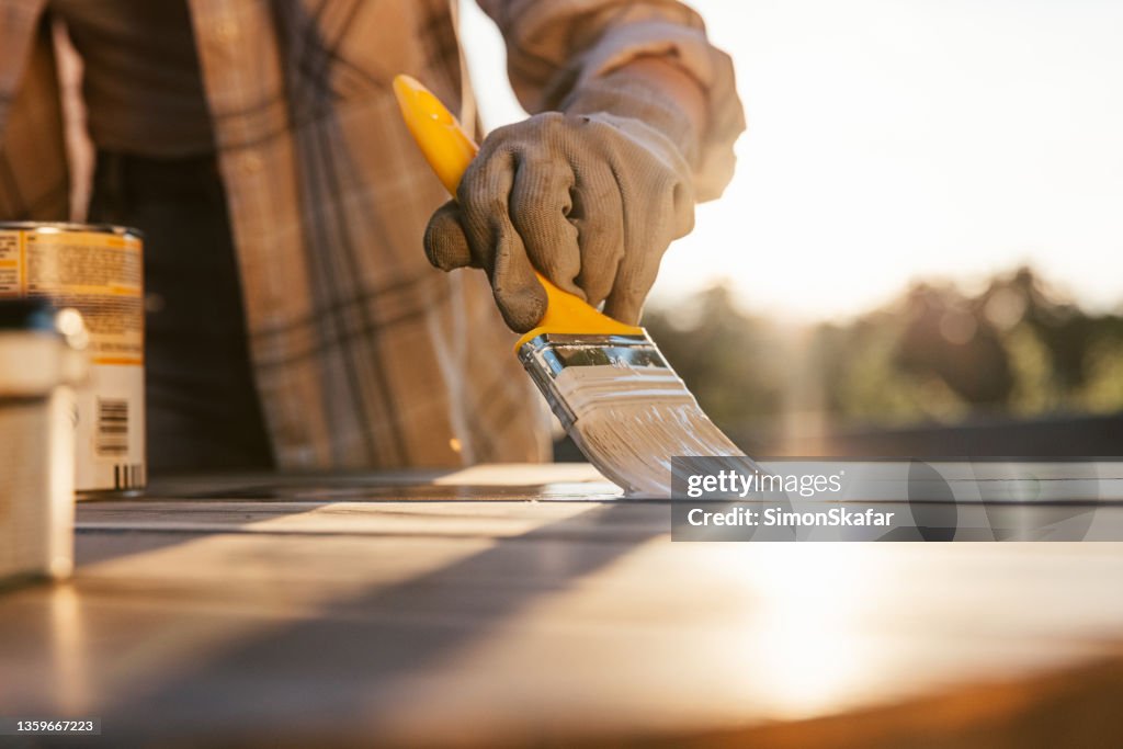 Close-Up woman with yellow brush,painting old wooden table with sun in background