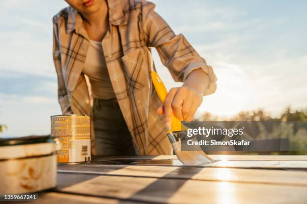 adult woman painting table with varnish using yellow brush - plank meubels stockfoto's en -beelden