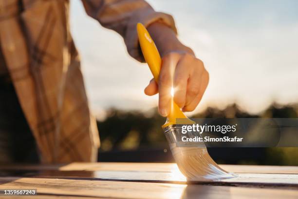 close-up yellow brush held by woman,painting table with fresh varnish sunbeam between fingers - paint brushes stock pictures, royalty-free photos & images