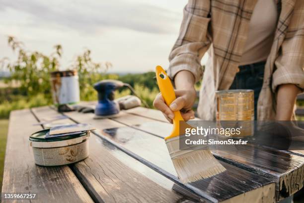 woman painting old table with a brush in the garden on a cloudy day - wood furniture stock pictures, royalty-free photos & images