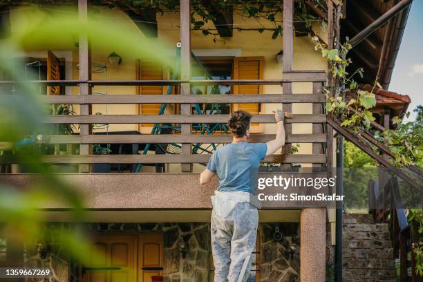 adult man painting wooden balcony fence at a house with a big brush - facade painting stock pictures, royalty-free photos & images