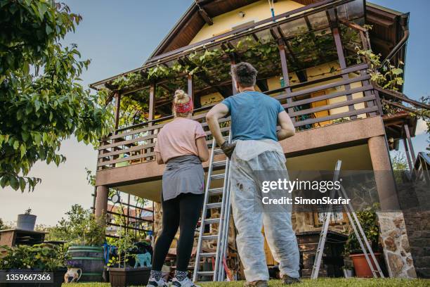 erwachsenes paar mit niedrigem winkel, das nach harter malerarbeit seinen balkonzaun überprüft - überholen stock-fotos und bilder