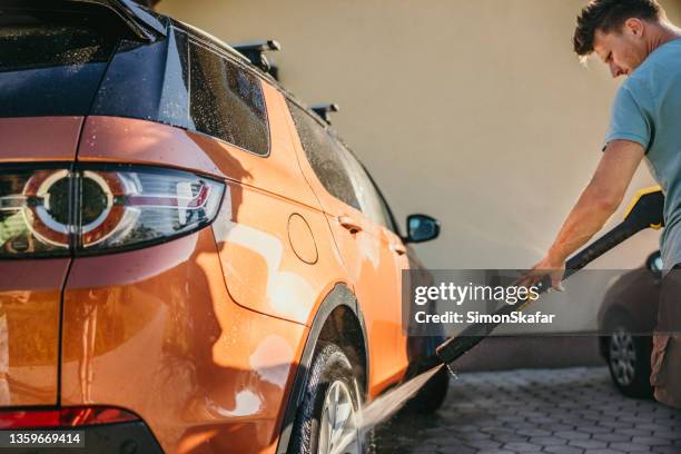 man with short brown hair and beard using high pressure cleaner to clean the rims of his car - car splashing water on people stock pictures, royalty-free photos & images