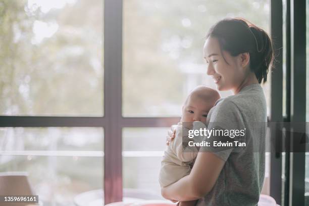 asian chinese mother carrying her baby boy from crib in the morning bonding time with backlit sunlight - hemmavarande förälder bildbanksfoton och bilder