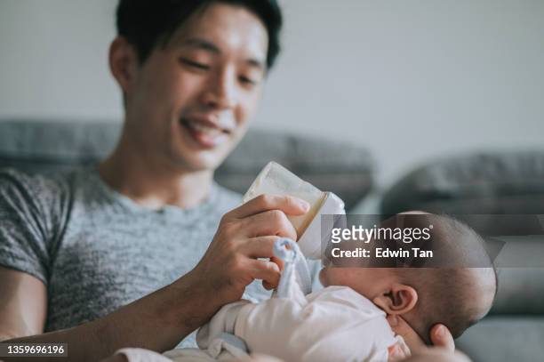 un jeune père chinois d’origine asiatique nourrit son petit garçon avec un biberon de lait dans le salon pendant le week-end - nourrir photos et images de collection