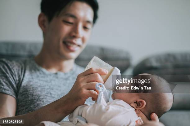 asian chinese young father feeding his baby boy son with milk bottle at living room during weekend - mjölkpulver bildbanksfoton och bilder