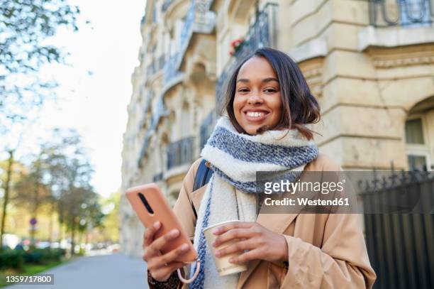 smiling woman with mobile phone and disposable cup in city - paris hiver photos et images de collection