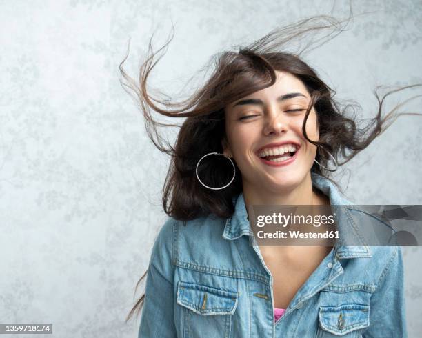 cheerful woman with tousled hair in front of wall - hair flying stock-fotos und bilder
