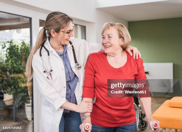 doctor helping disabled woman standing with crutch at home - orthopädie stock-fotos und bilder
