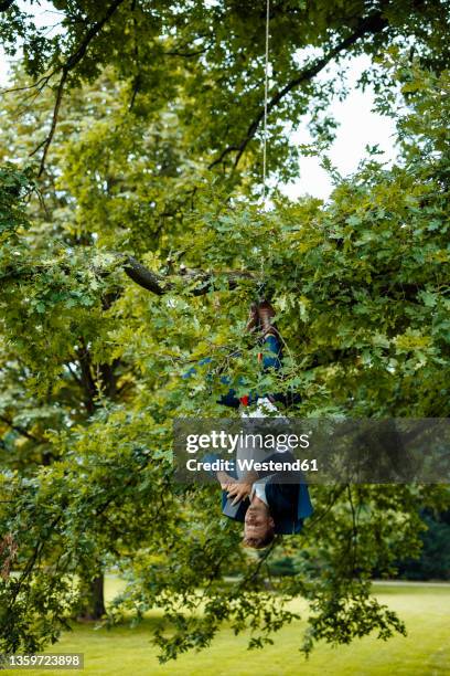 businessman hanging upside down with rope from tree using mobile phone at park - smartphones dangling stock pictures, royalty-free photos & images