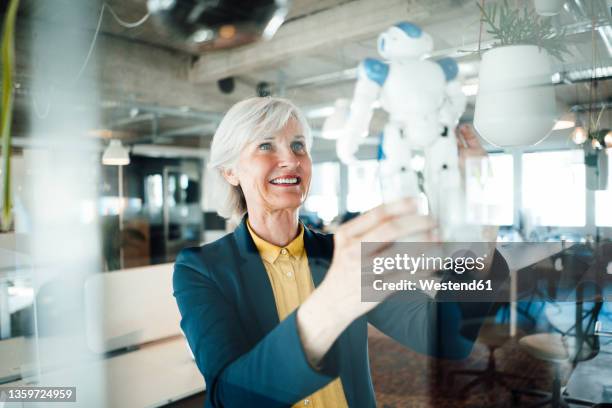 senior businesswoman holding robot toy in office - robotics alive stock pictures, royalty-free photos & images