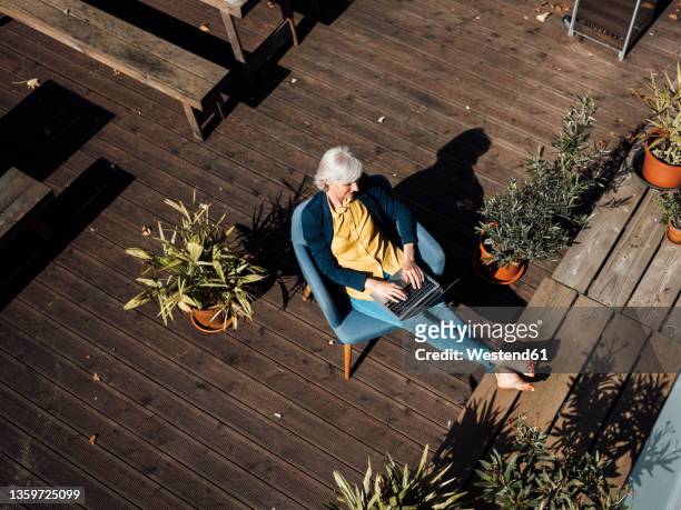 businesswoman using laptop at rooftop on sunny day - eine seniorin allein stock-fotos und bilder