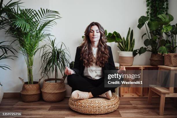 businesswoman meditating by plants in office - lotuspositie stockfoto's en -beelden