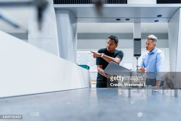 engineer with laptop pointing by businessman at factory - fließbandfertigung stock-fotos und bilder